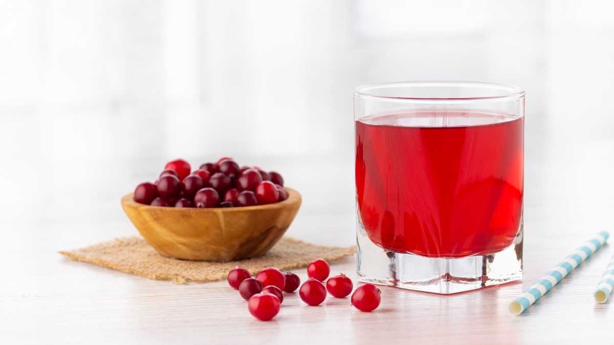 Um copo de suco de cranberry ao lado de uma tigela de cranberries e um canudo azul