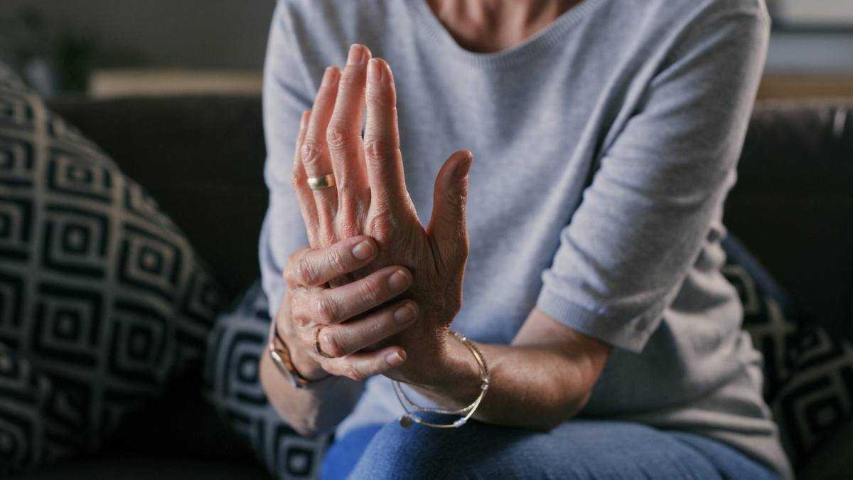 en närbild av en kvinna som håller hennes hand med ledvärk, vilket kan dra nytta av vitlök och honung