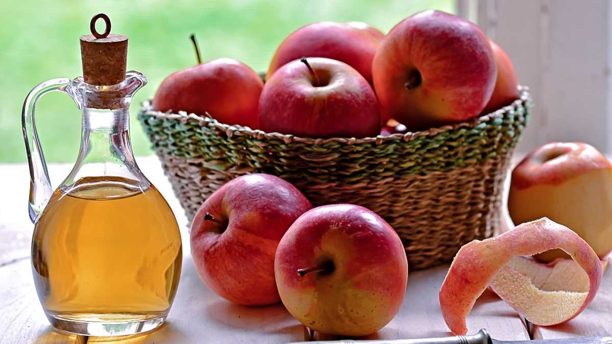 Uma garrafa transparente de vinagre de maçã ao lado de uma cesta de maçãs vermelhas