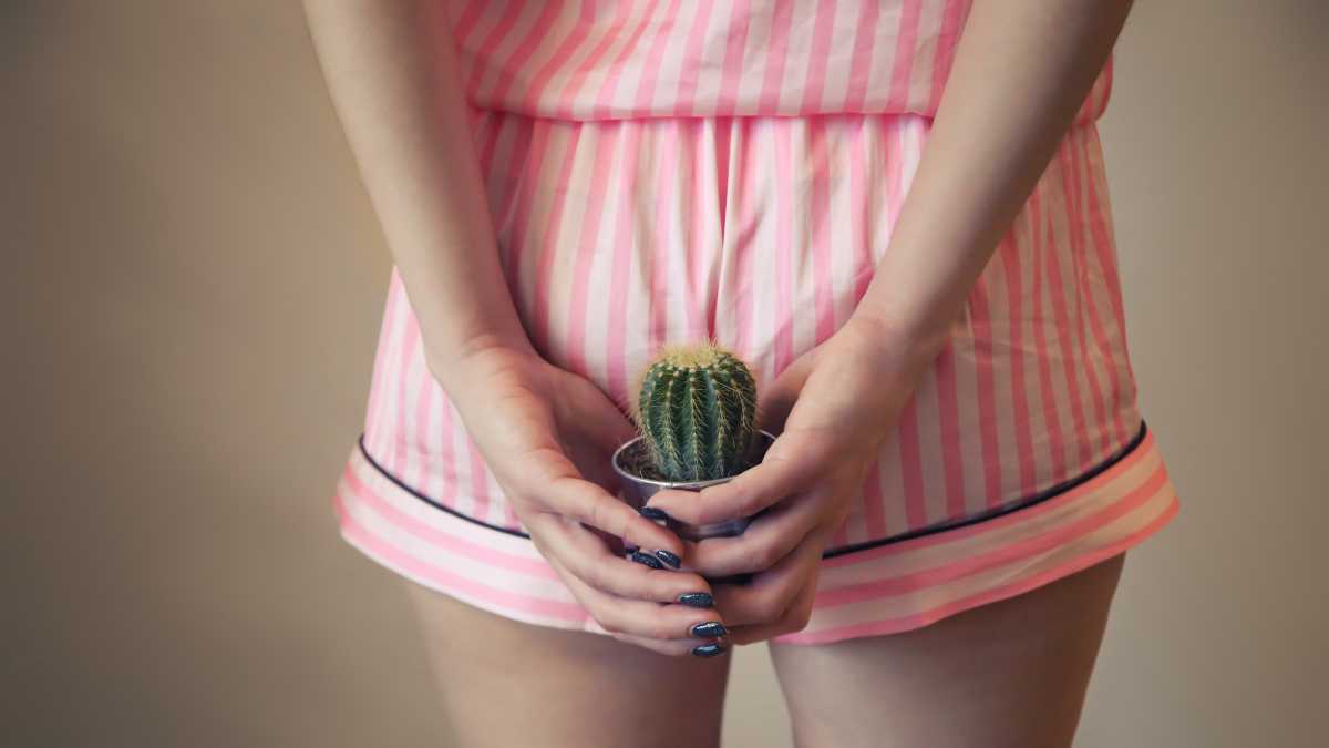 Zbliżenie kobiety w różowej piżamie w paski, trzymającej kaktusa za tyłkiem, aby zilustrować swędzenie hemoroidów