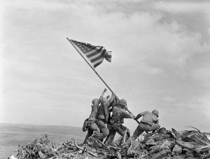 Ira Hayes stojí nalevo s nataženými pažemi, aby vztyčil americkou vlajku