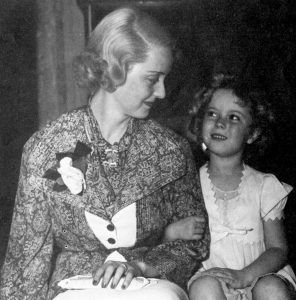 Bette Davis zit met een jonge Shirley Temple.