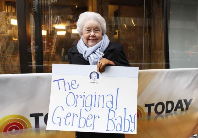 Ann Turner Cook con in mano un cartello che dice: The Original Gerber Baby
